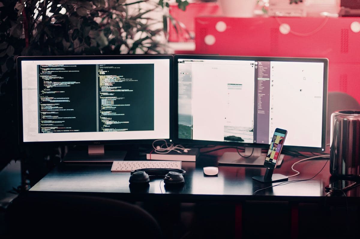 Two computer monitors on a desk with a keyboard and mouse positioned in front of them.