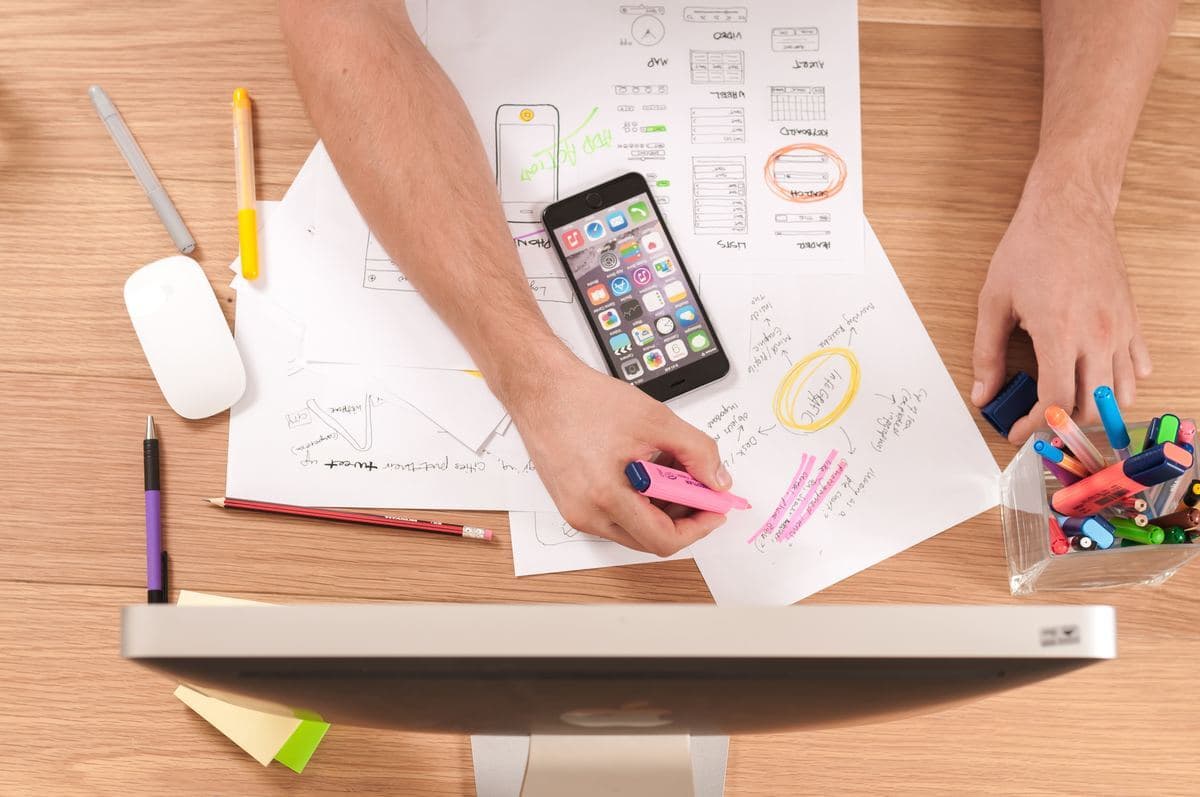 A person is using a cell phone while sitting at a desk, with various office supplies visible around them.