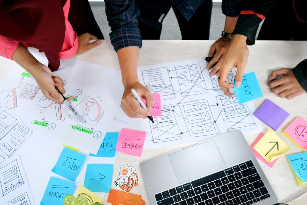 A diverse group of people collaborating around a laptop covered in colorful sticky notes.